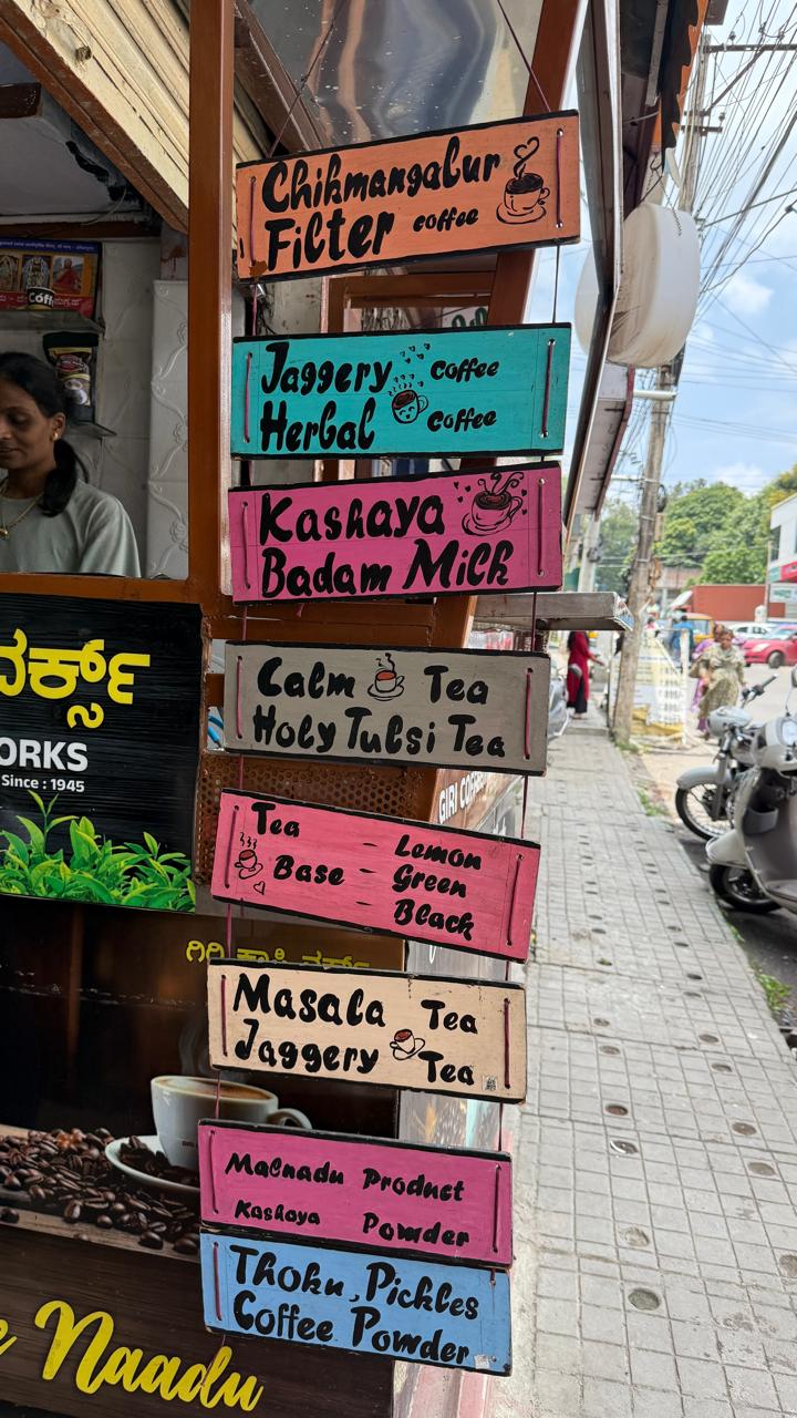 Hand-painted boards at the Giri Coffee Works counter listing the range — Chikmagalur filter coffee, jaggery & herbal coffee, kashaya, badam milk, masala tea and Malnadu products